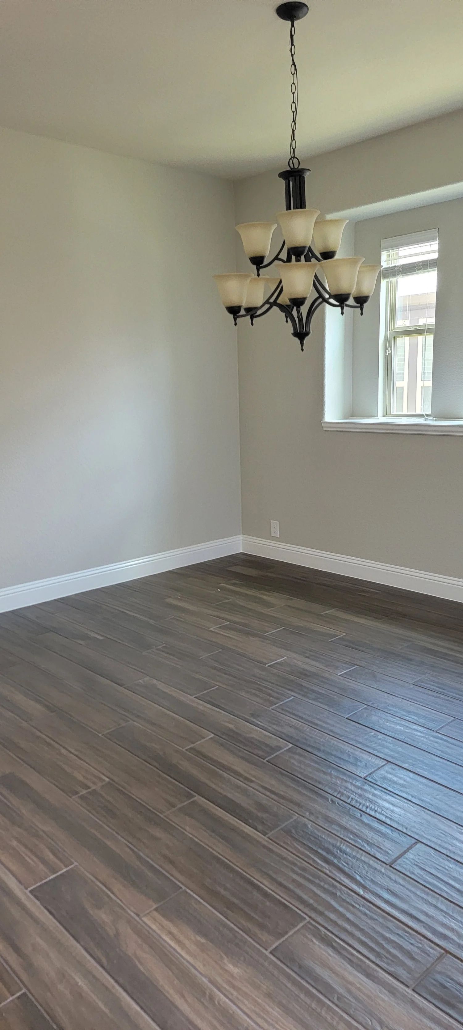 Empty room with wood-look tile floor, a chandelier, and a window.