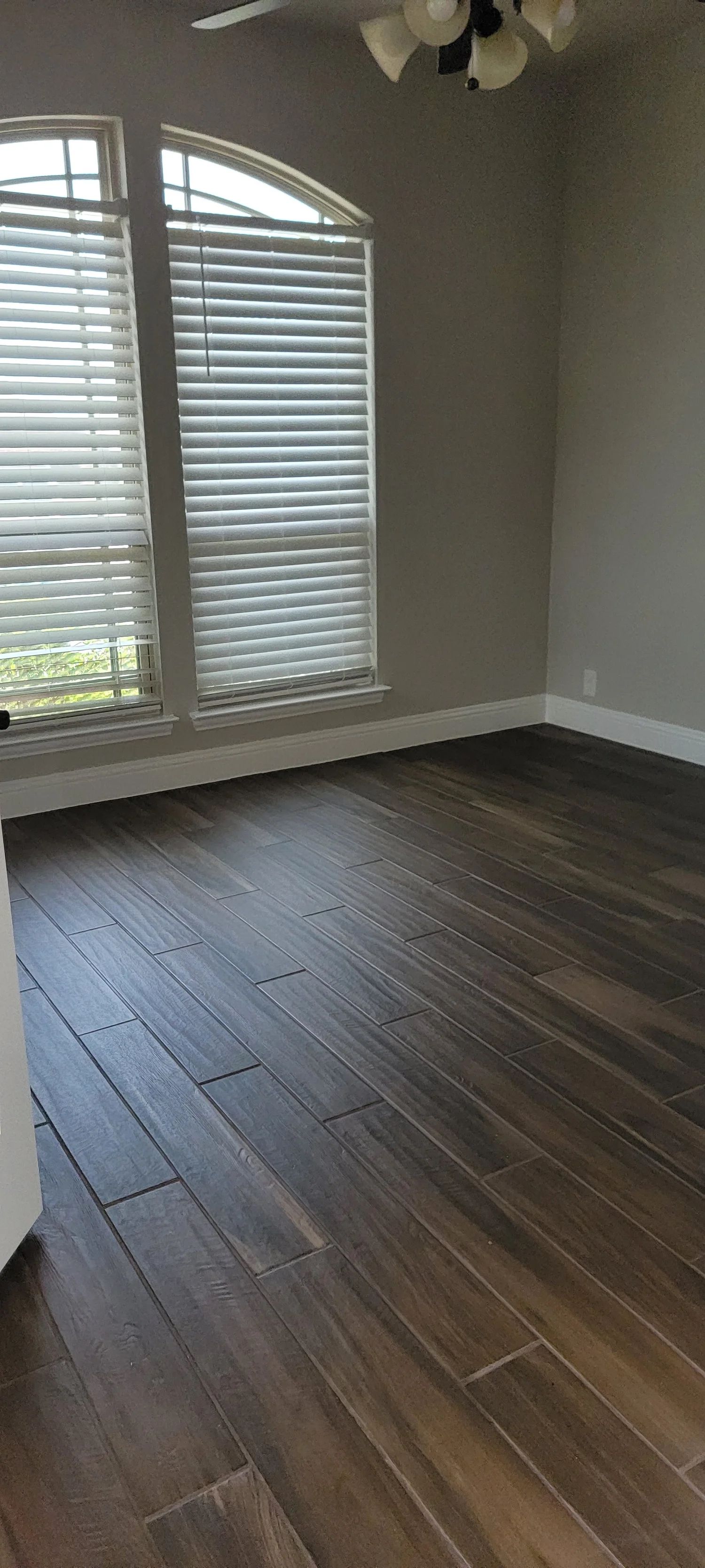 Room with dark wood-look flooring, large window with blinds, and neutral walls.
