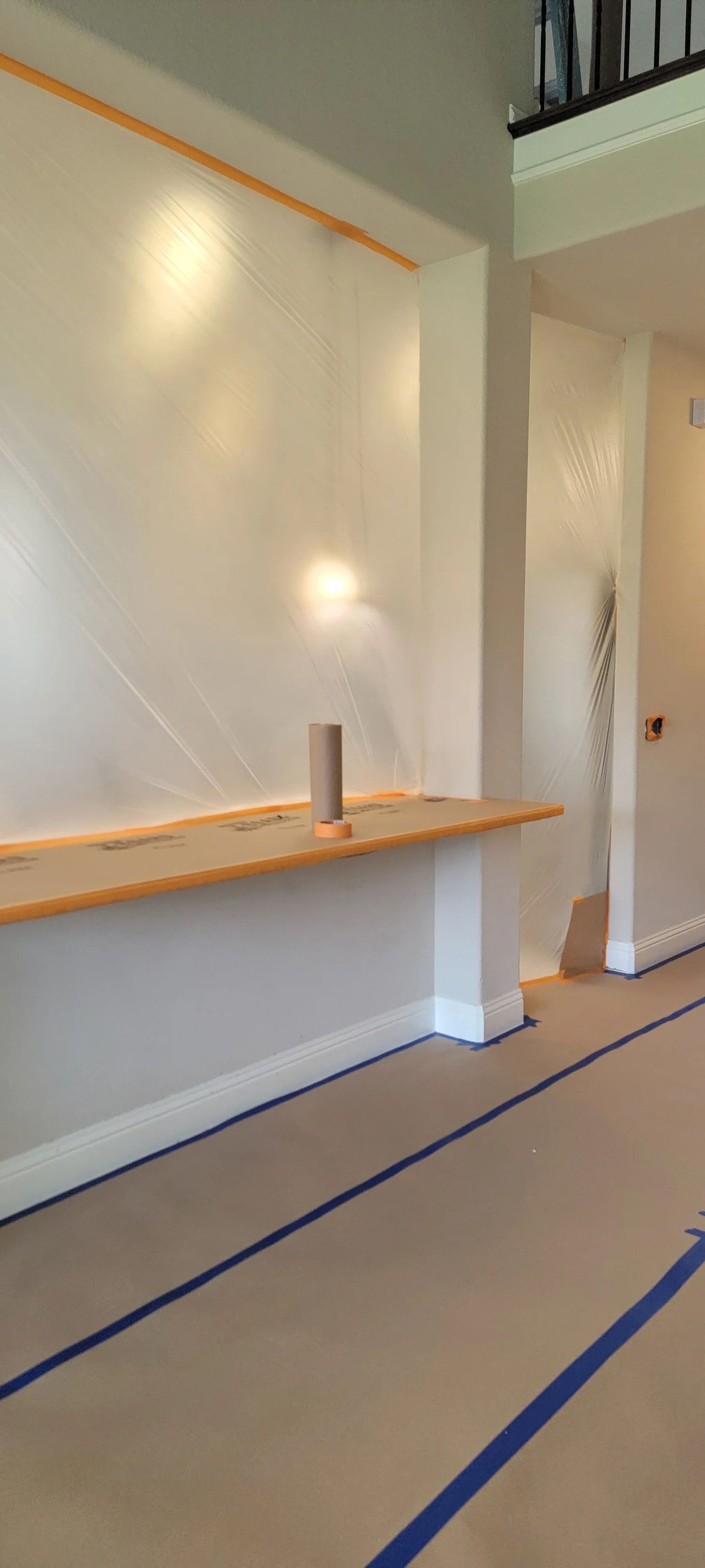 Interior room renovation; walls covered in plastic, blue tape on the floor.