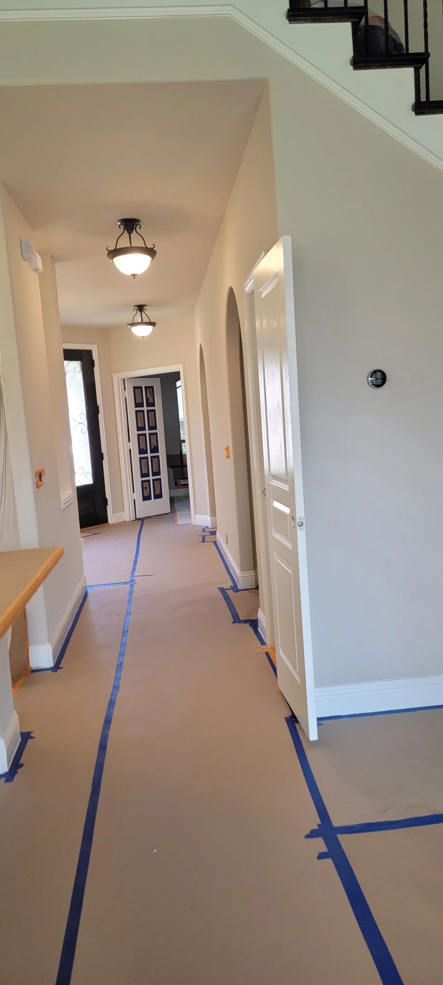 A hallway undergoing renovation with protective paper and blue tape on the floor. White doors and light fixtures.