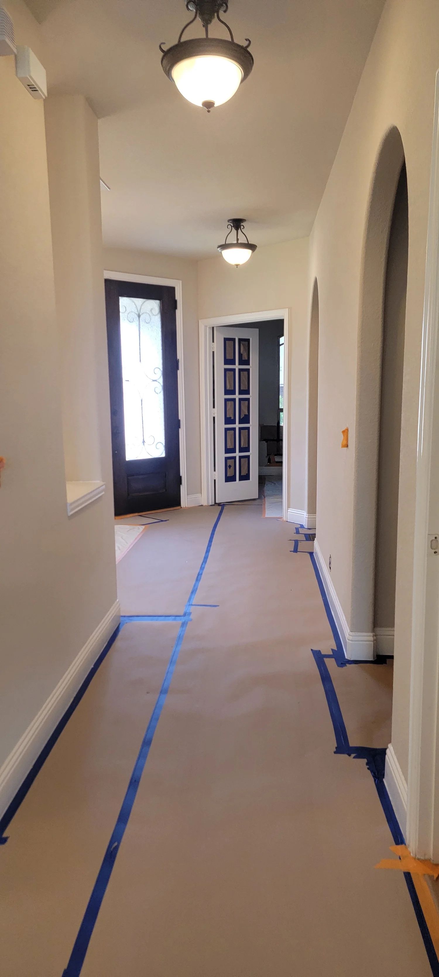 Hallway with beige walls, brown floor covering, blue tape, and two ceiling lights.