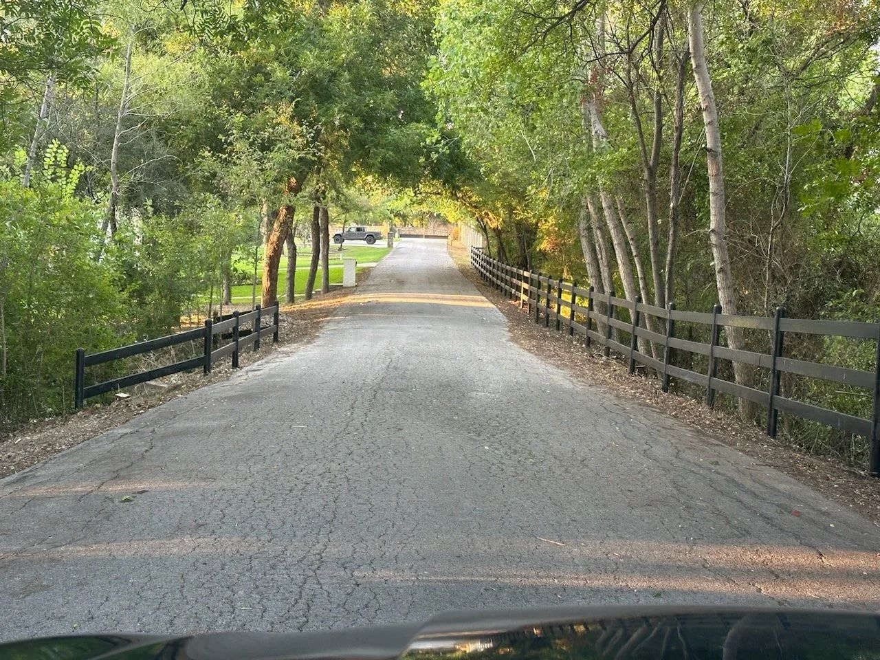 A gravel road flanked by a black fence and trees, leading into the distance.