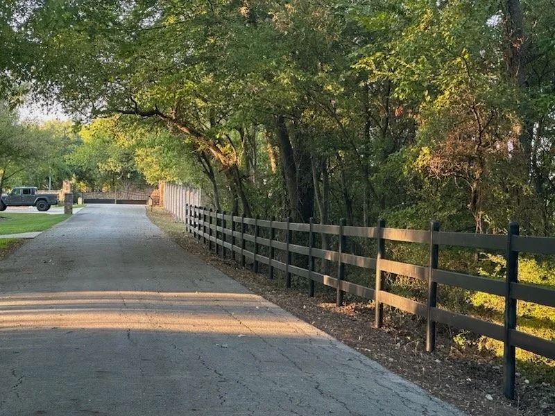 Asphalt road with dark wooden fence and trees on either side.