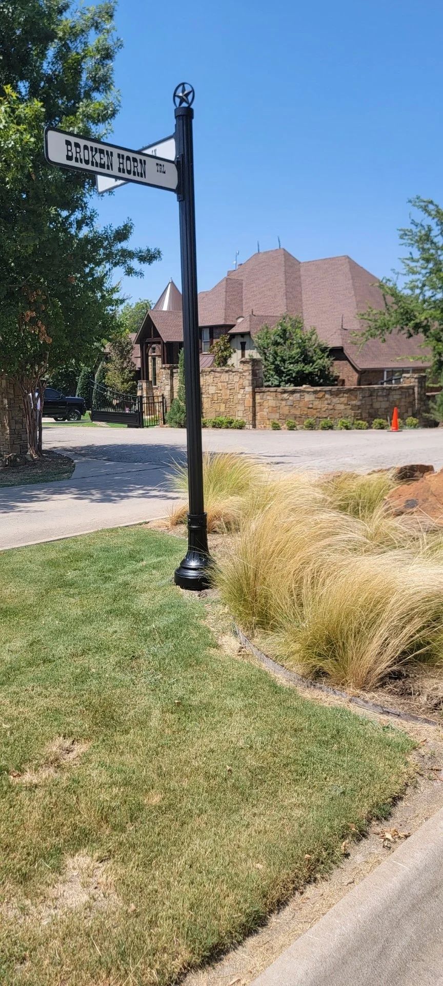 Street sign in front of a large house with a brown roof. Green grass and blue sky.