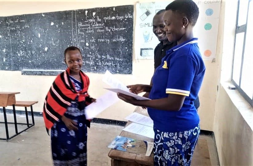 A Makat village student receiving an English certificate from her teachers in a schoolhouse.