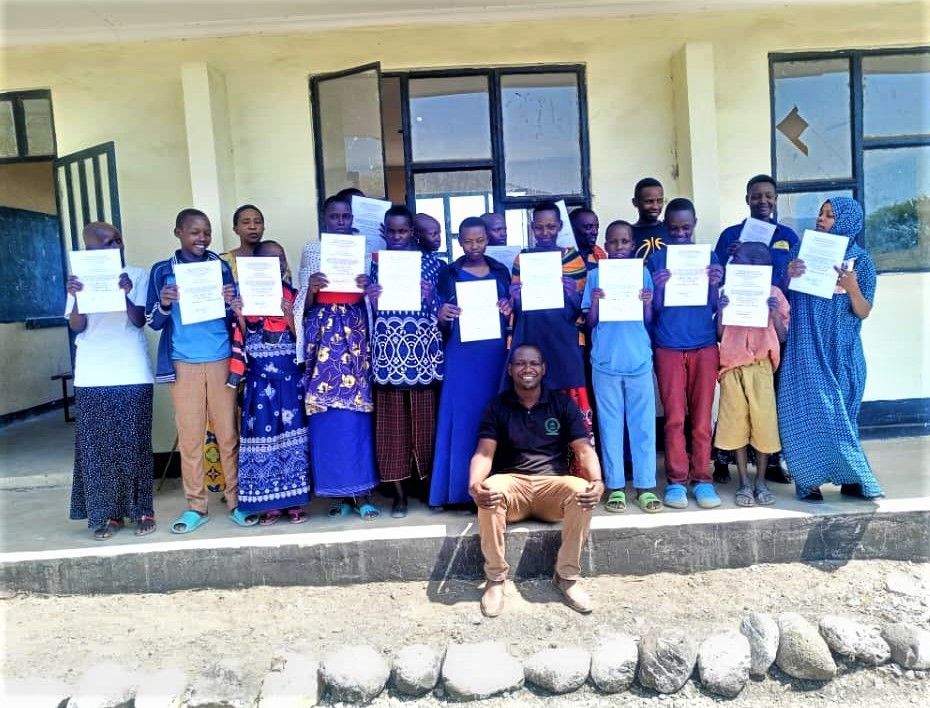 A group of Makat village students standing in front of a schoolhouse holding certificates.