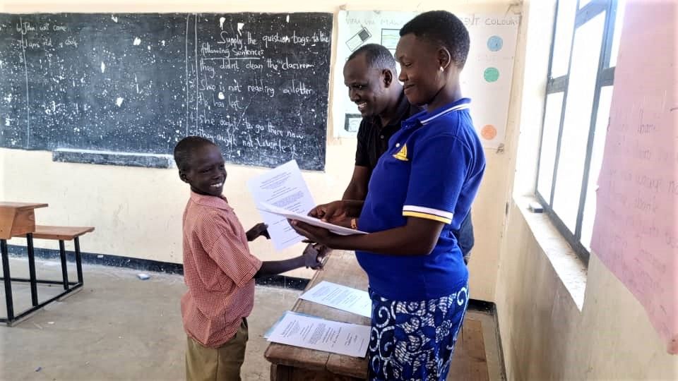 A Makat village student receiving an English certificate from his teachers in a schoolhouse