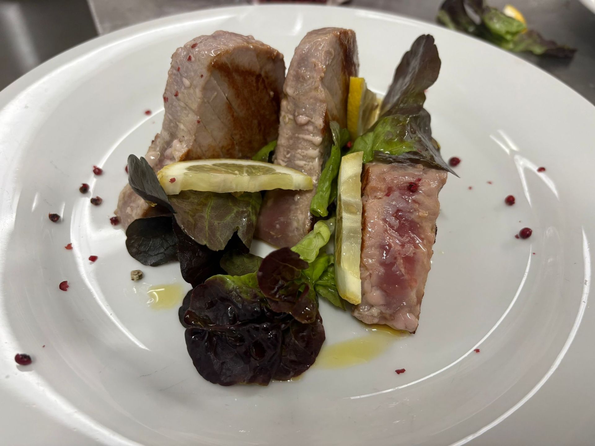 Carne scottata servita su un piatto bianco con verdure e salsa scura.