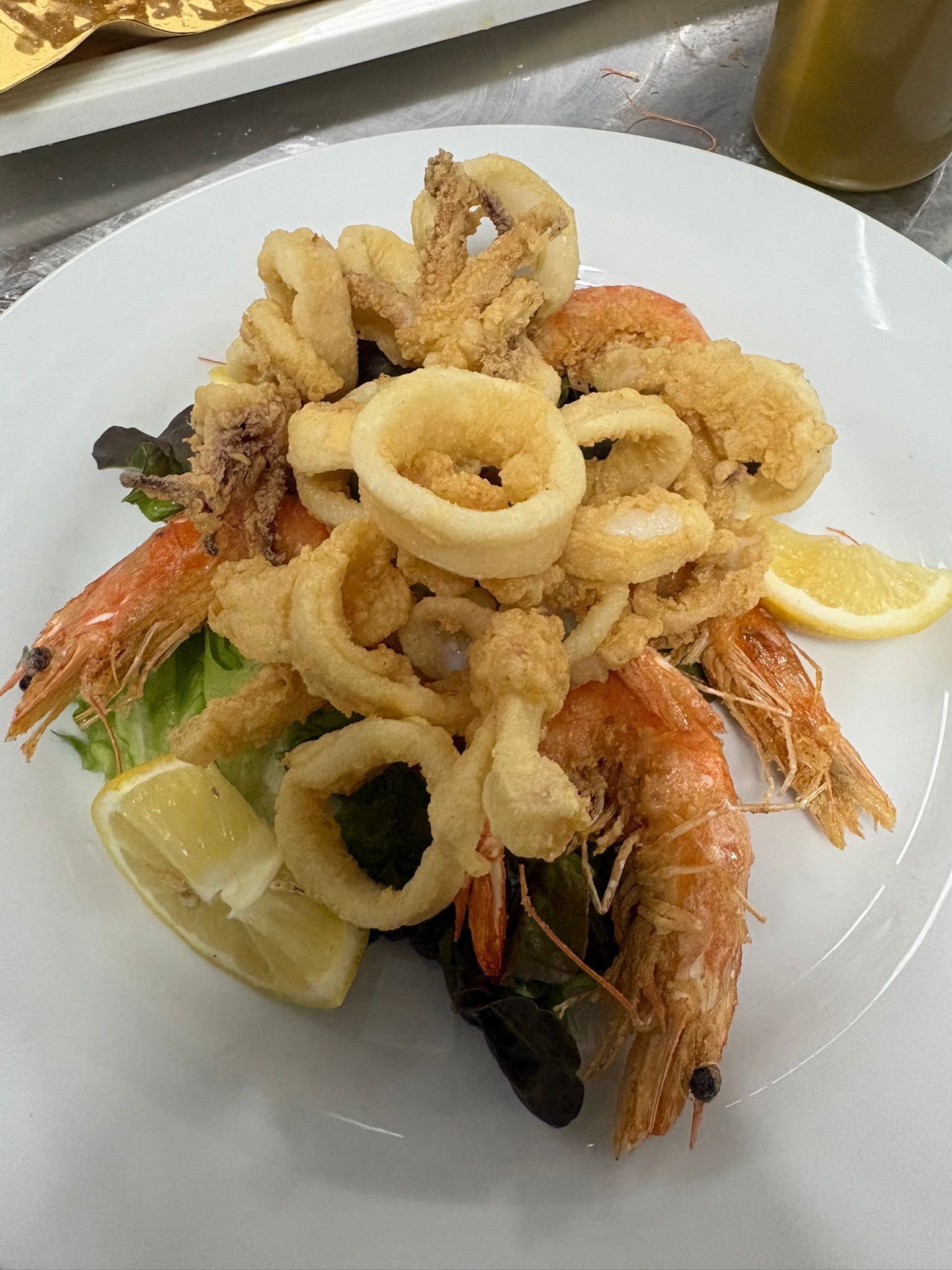 Piatto di frutti di mare con calamari fritti, gamberi, spicchi di limone e prezzemolo su un piatto bianco.