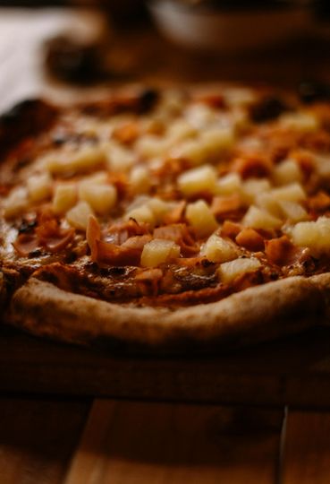 Primo piano di una pizza con ananas a cubetti su un tavolo di legno.