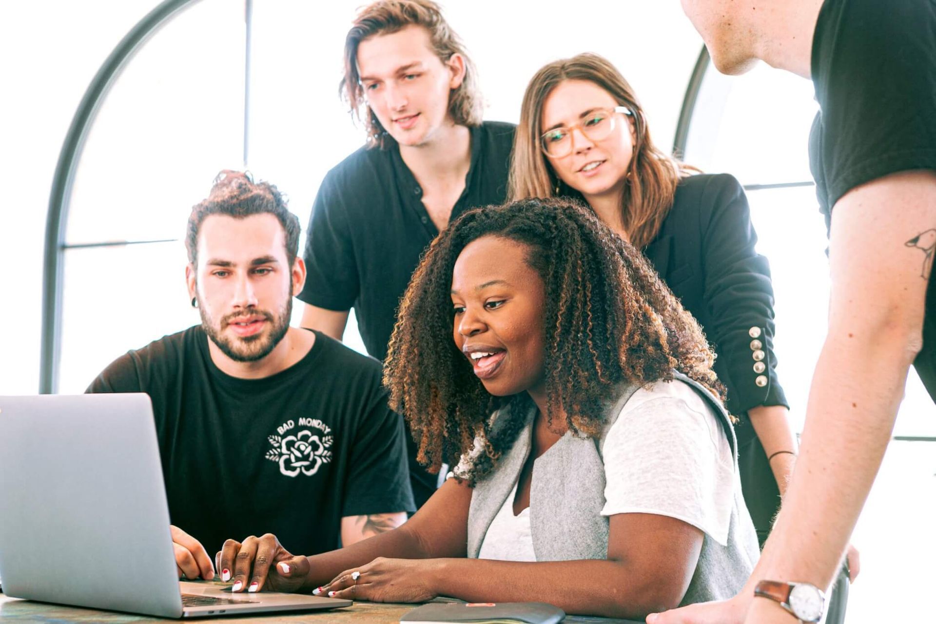 Equipe de pessoas olhando para a tela de um laptop; reunião colaborativa em um escritório moderno.