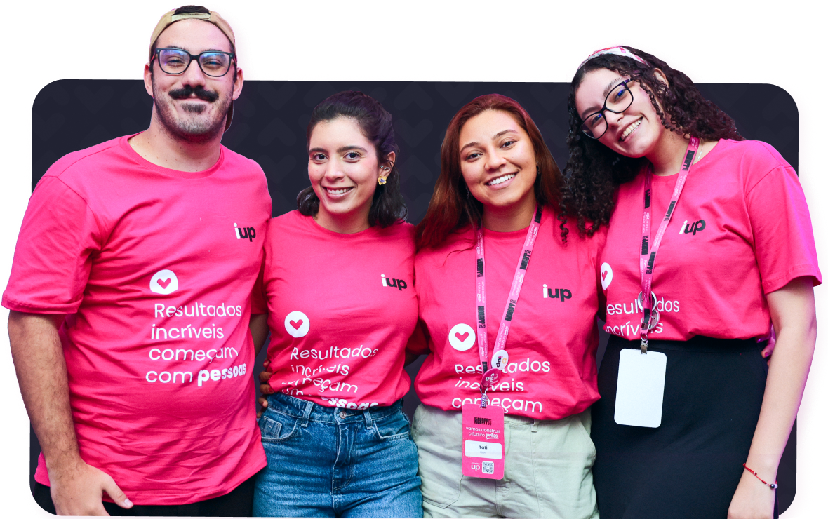Quatro pessoas vestindo camisetas rosa-choque do evento, posando juntas em um ambiente interno e sorrindo para a câmera.