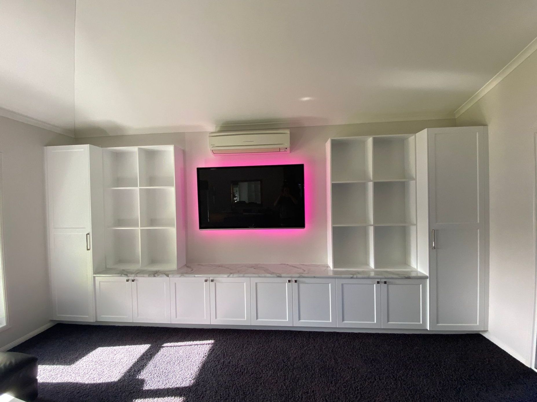 White built-in entertainment center with TV, open shelves, cabinets, and pink LED light, set against a white wall. — Cut N Edge Panel Factory In Coolum Beach, QLD
