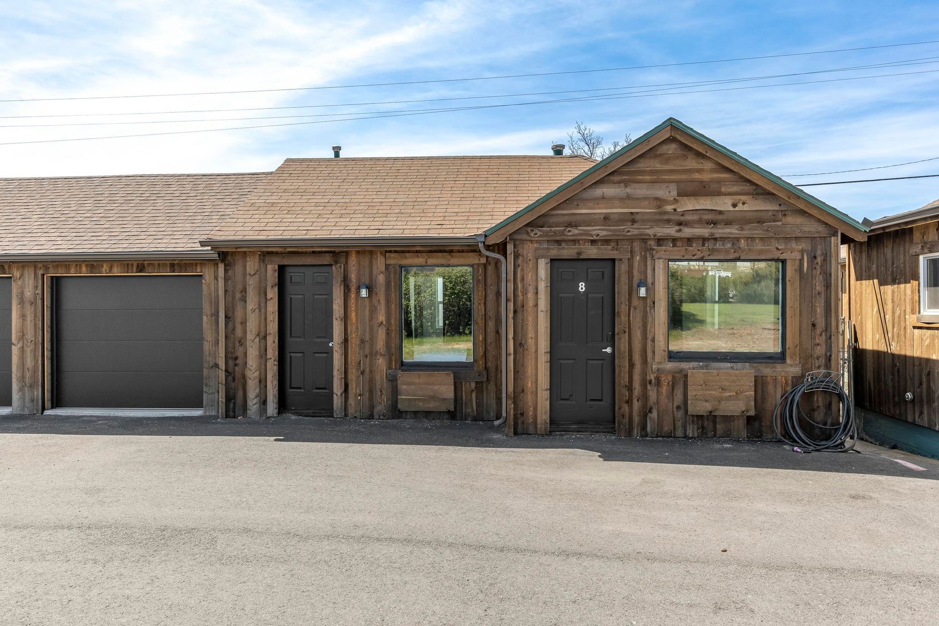 Rustic wooden building with garage door, windows, and two entry doors under a blue sky