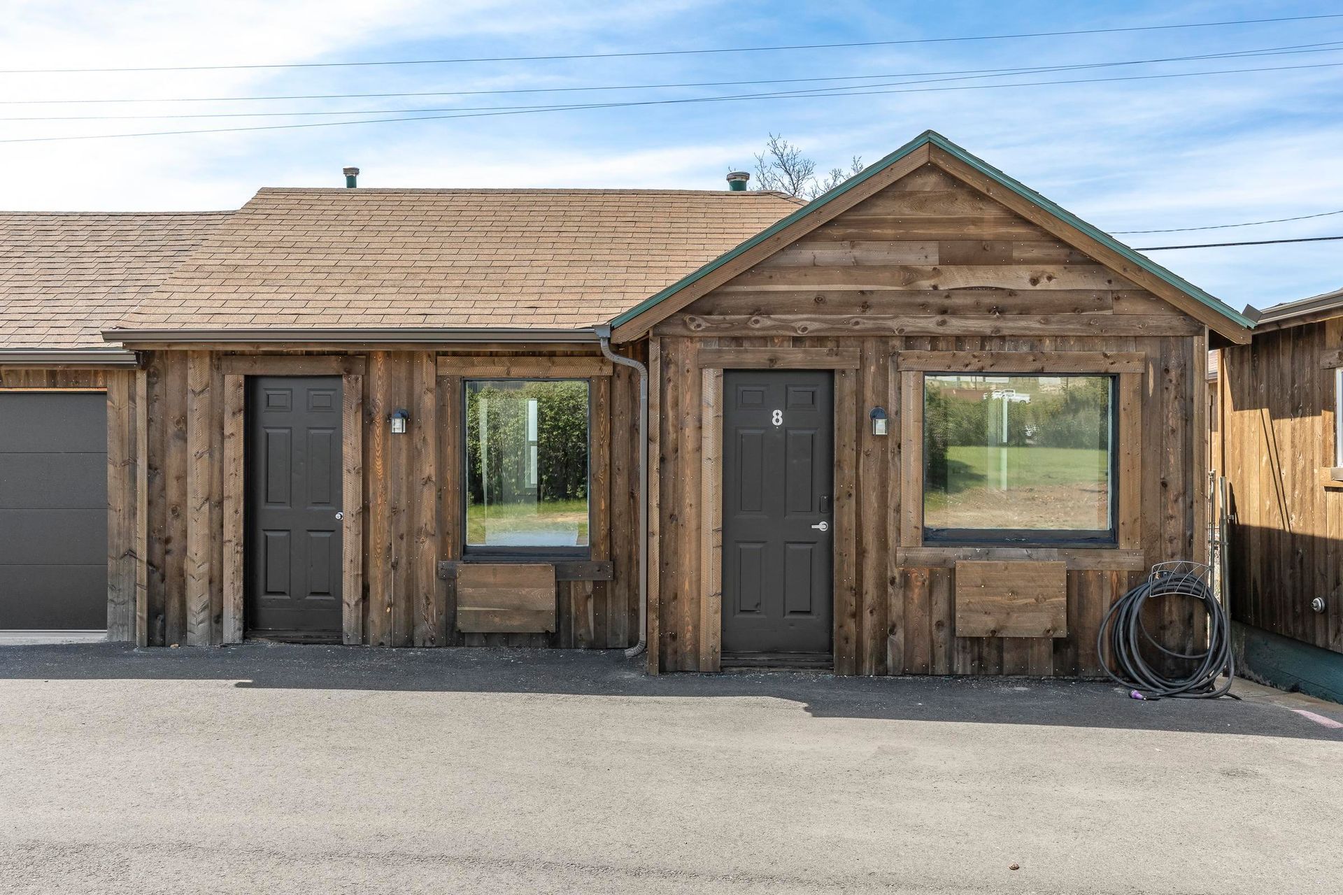 Single-story wooden duplex with two front doors and large windows under a clear sky