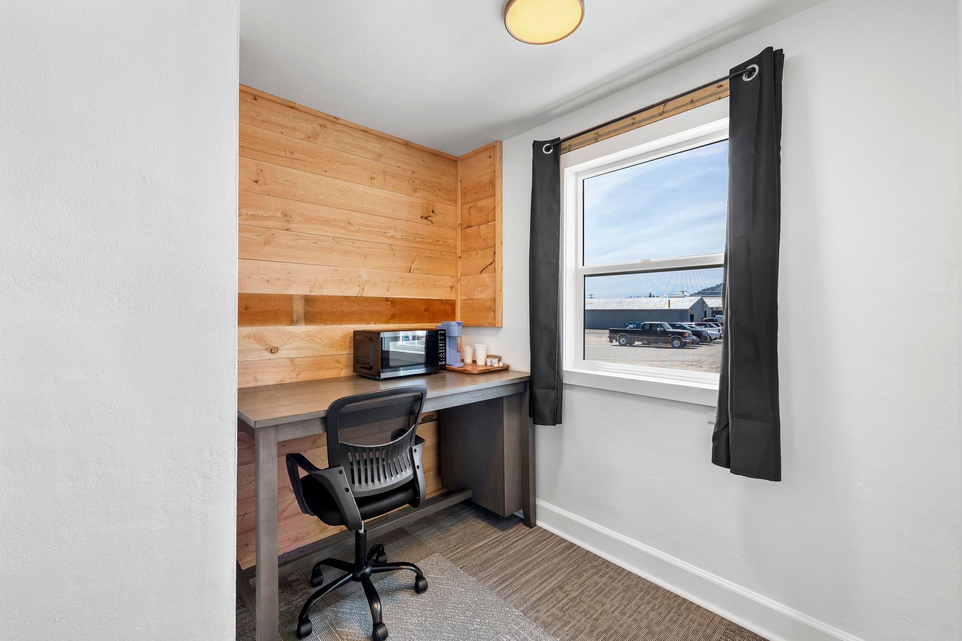 Small home office with a desk, black chair, wood-paneled wall, and window overlooking water.