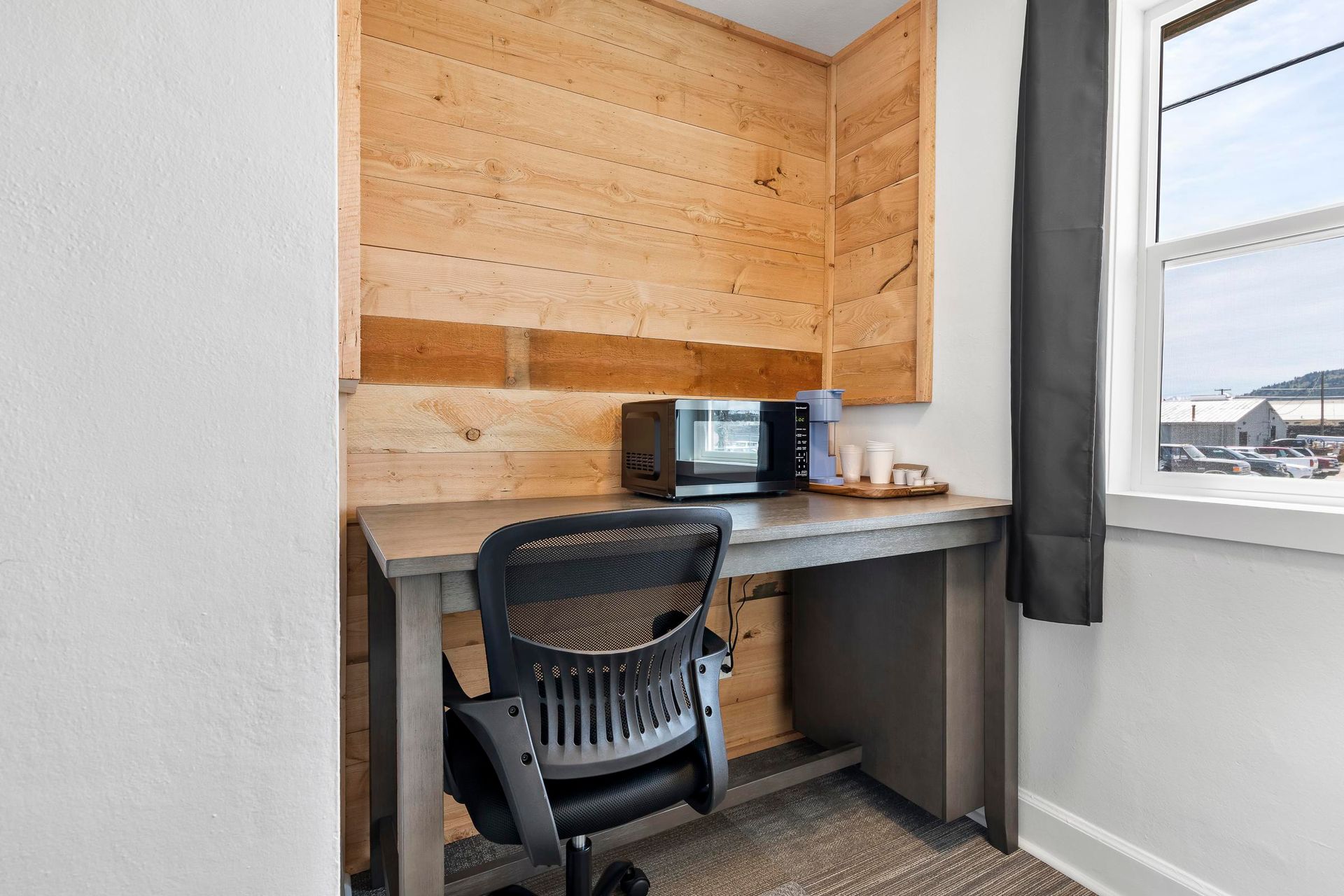 Small home office nook with desk, chair, monitor, wood paneling, and a window with gray curtains.