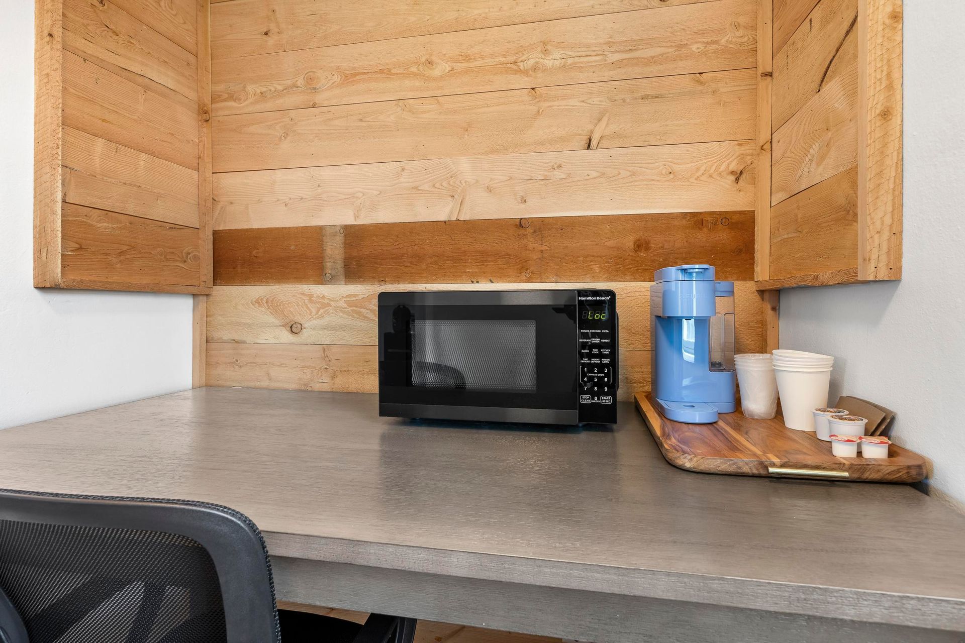 Small kitchenette counter with a microwave and water dispenser beside paper cups and a tray