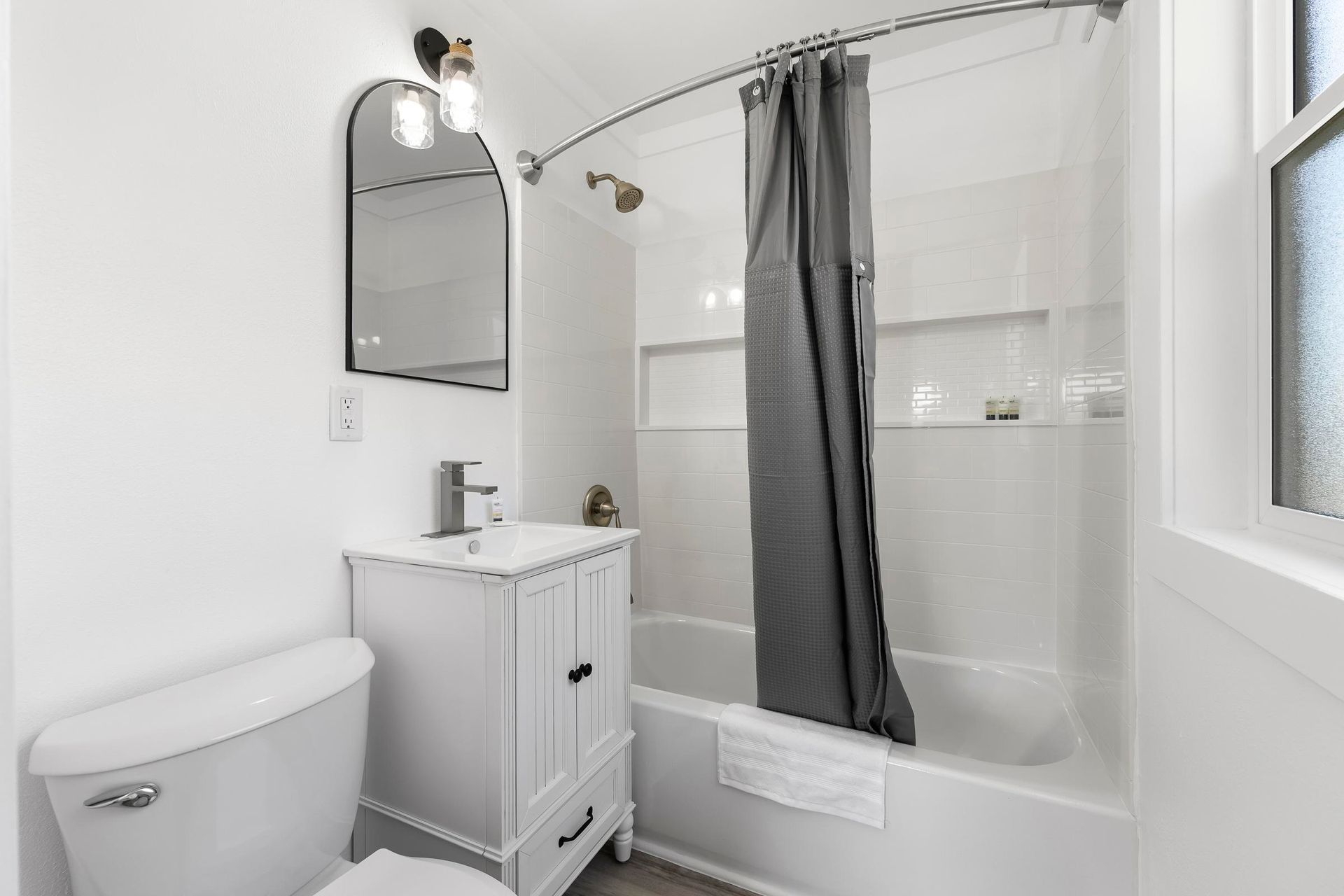 Bright white bathroom with toilet, vanity, mirror, and shower-tub with gray curtain