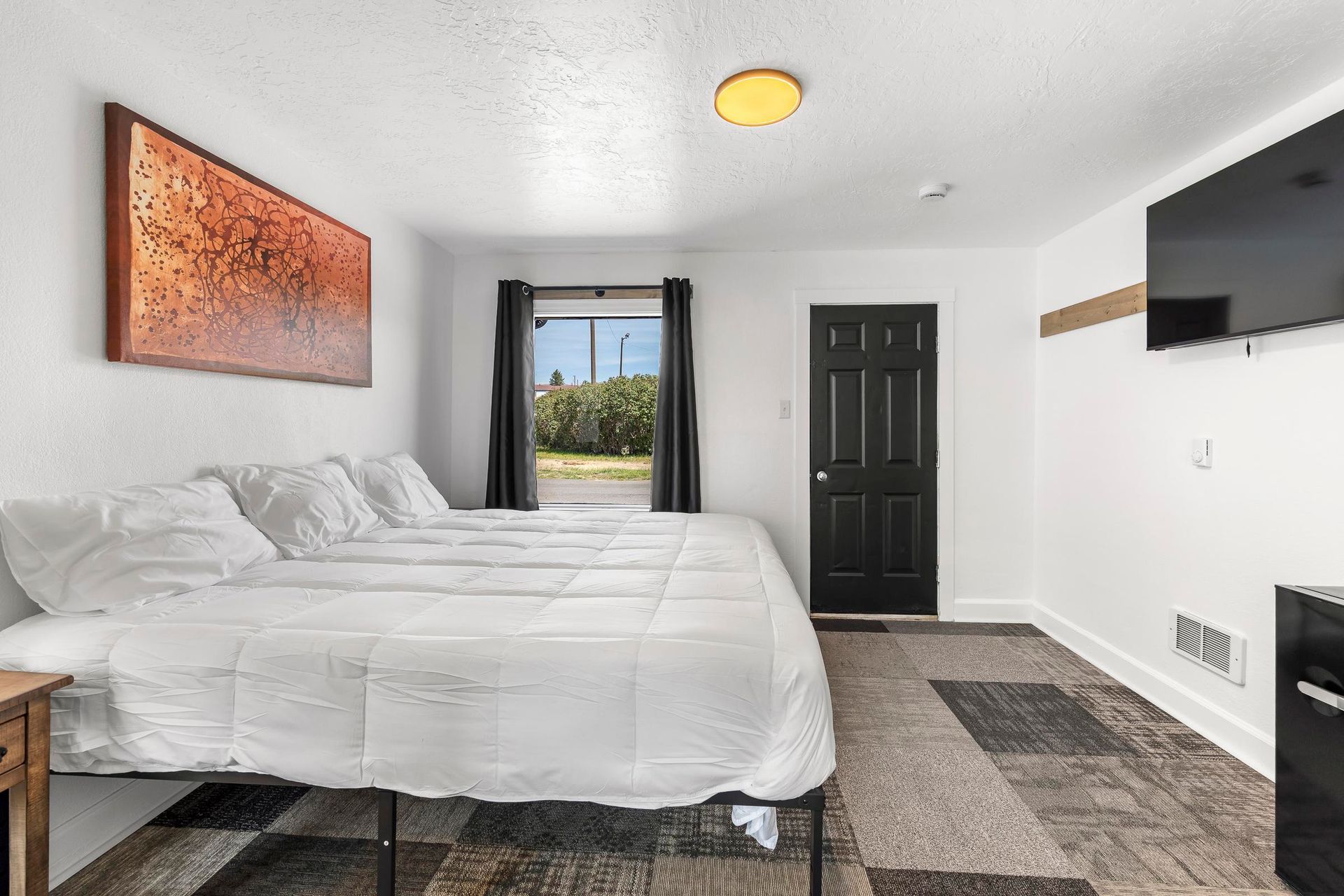 Bright bedroom with white bed, black door, wall art, TV, and view through balcony doors