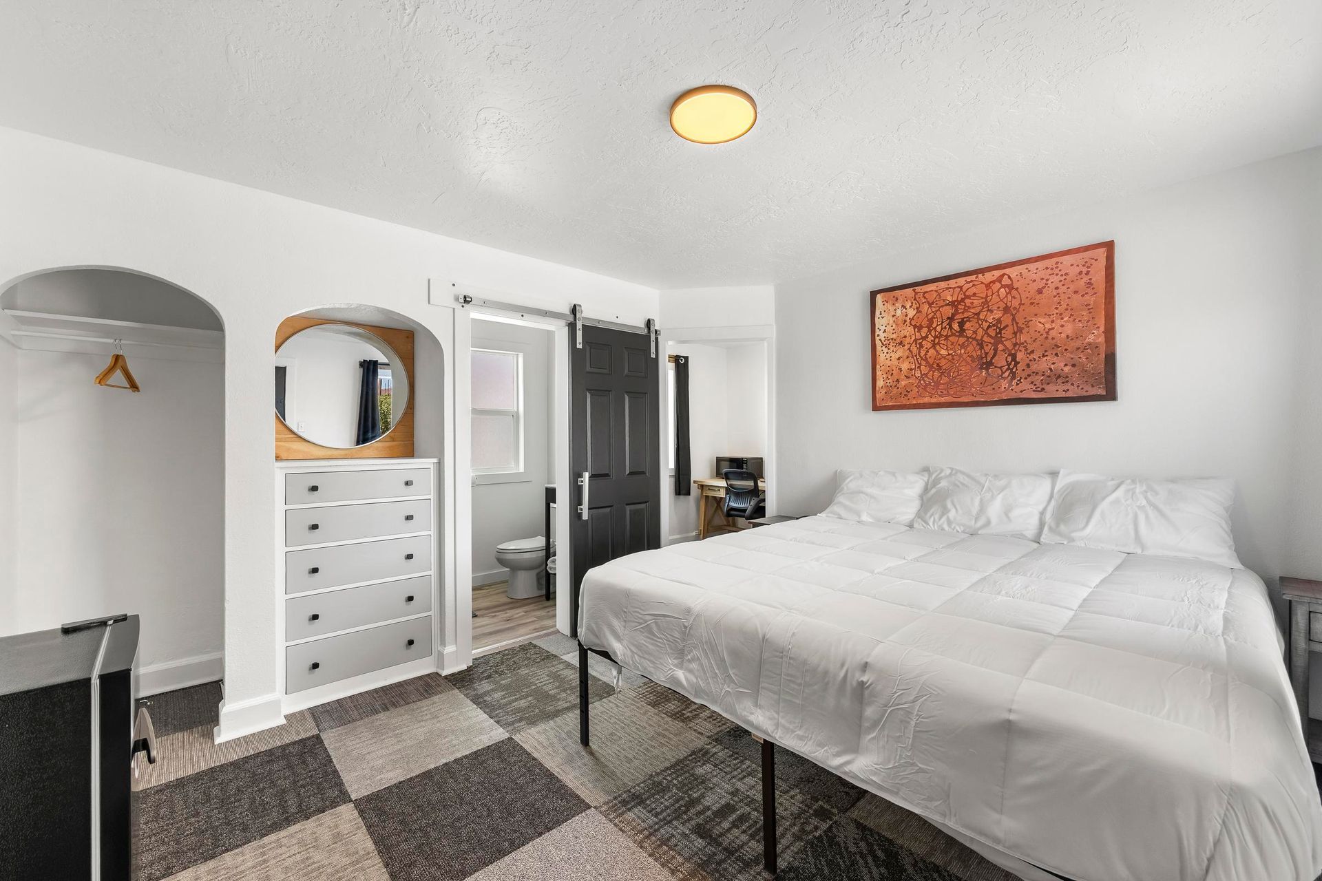 Bright bedroom with a white bed, dresser, mirrored closet, and patterned rug.