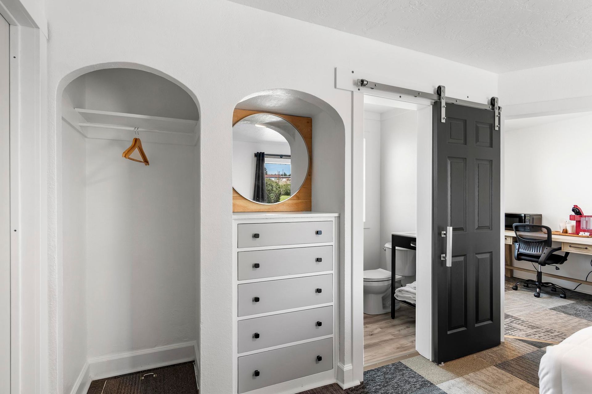 Bright bedroom with open closet, white dresser, black door, and a desk in the background.