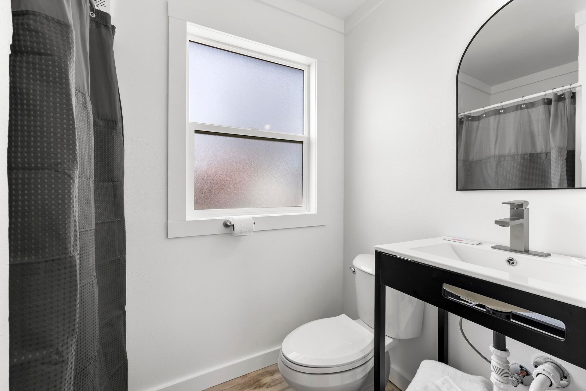 Small bathroom with frosted window, toilet, sink, mirror, and shower curtain.