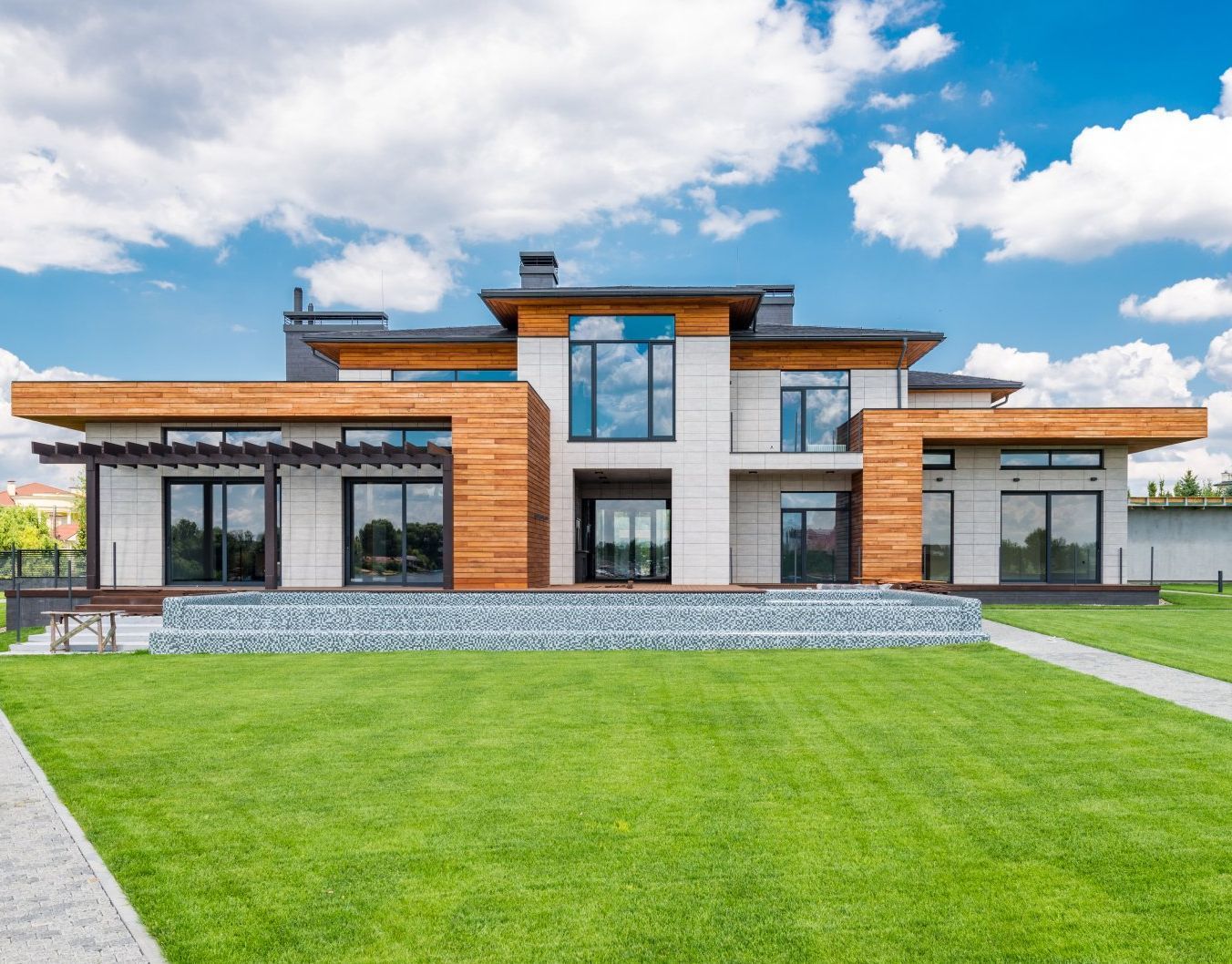 Modern flat-roof house with wood and white exterior, large windows, and a green lawn under a blue sky.
