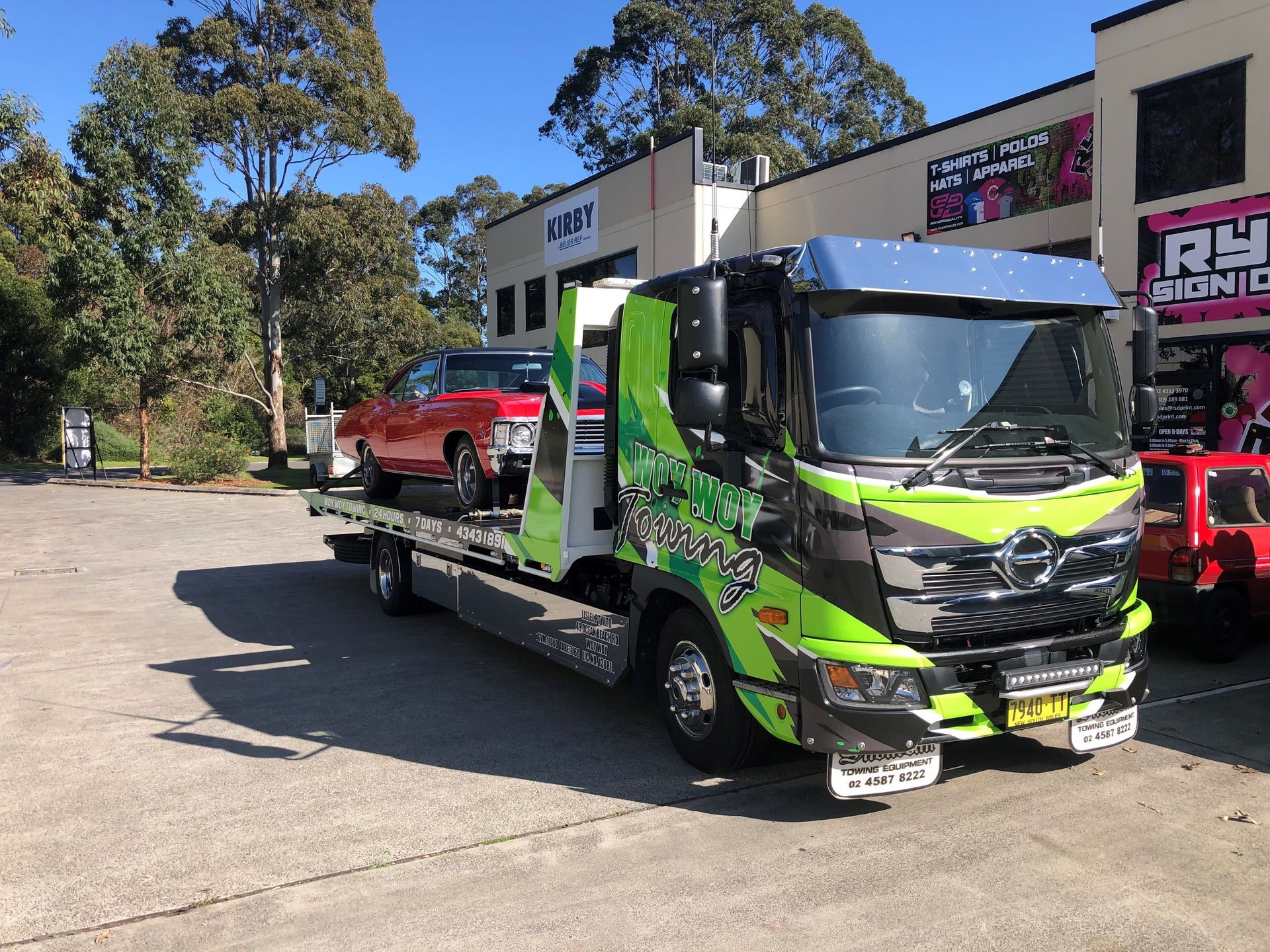 A man is standing next to a tow truck with a van on it.