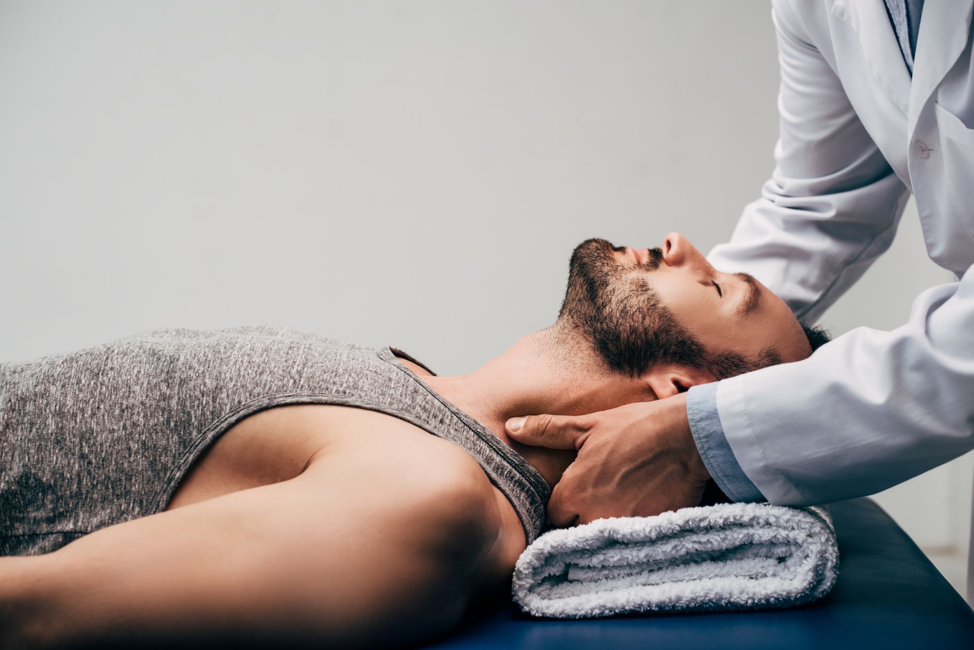 A man is laying on a table getting a neck massage from a doctor.