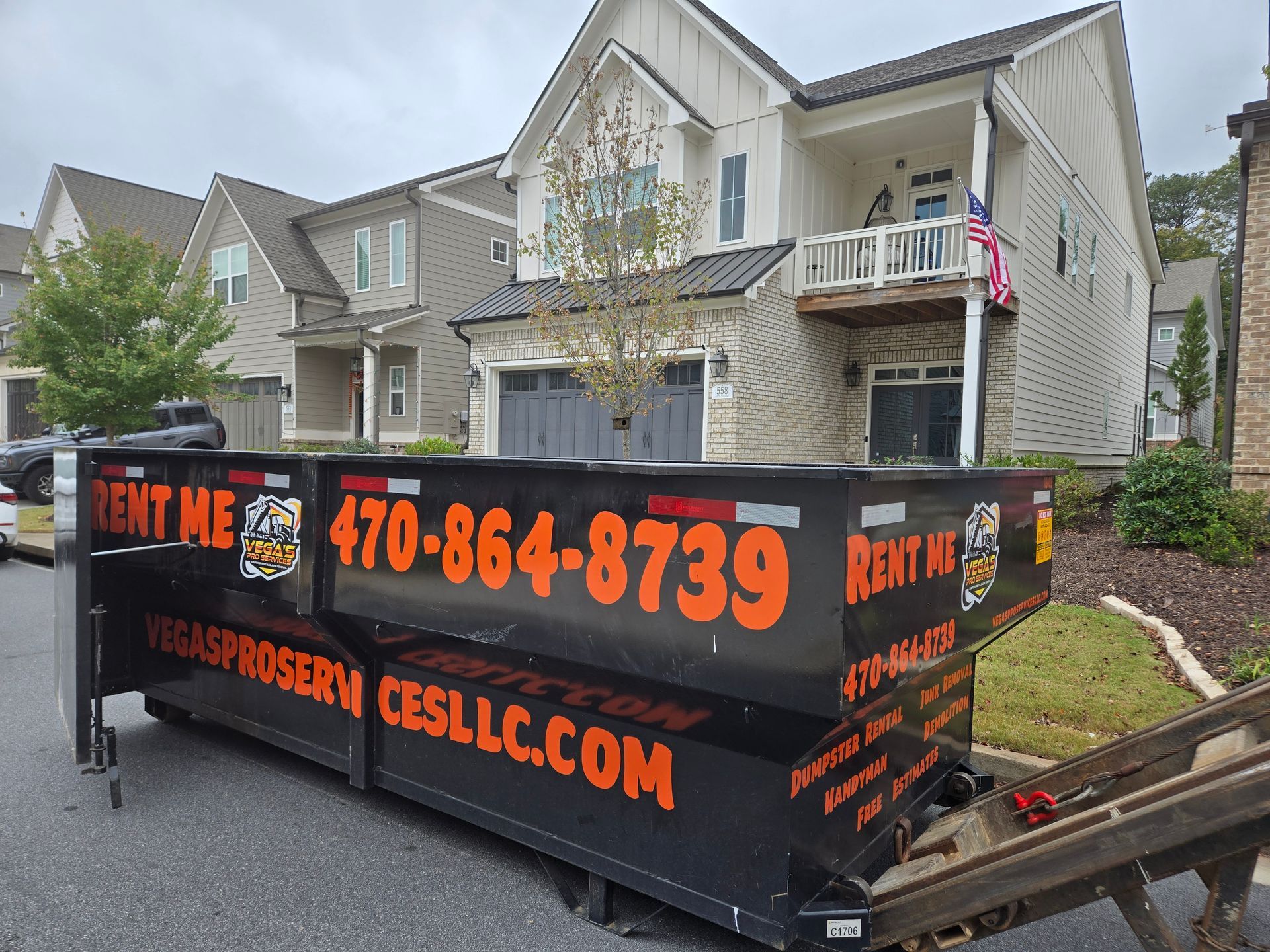 Black dumpster in front of a house, with a phone number and website visible.