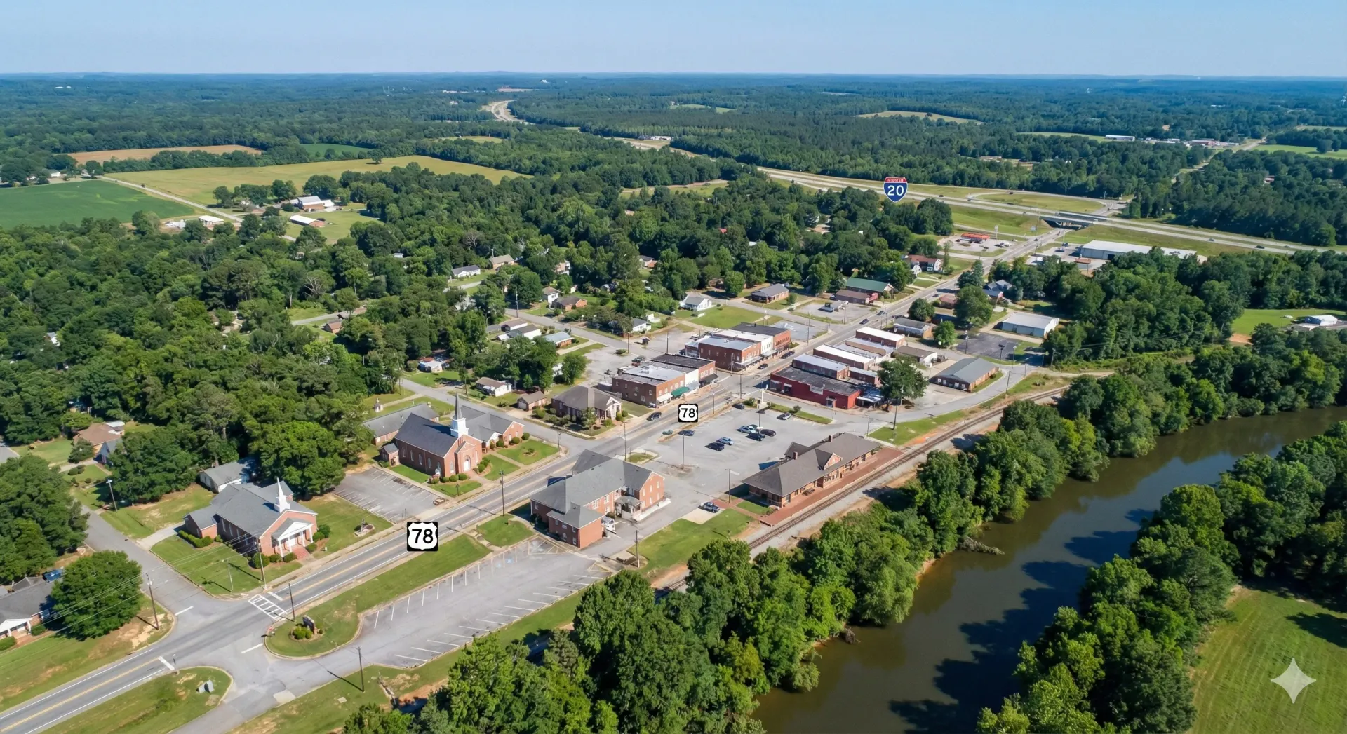 Aerial view of a small town with brick buildings, trees, and a river on a sunny day.