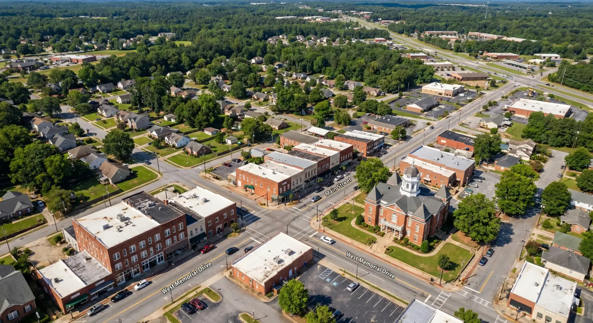 Aerial view of a small town with brick buildings surrounding a town square, green trees, and houses.