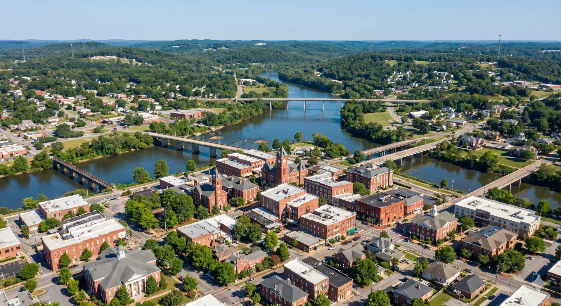 Aerial view of a town with red brick buildings, bridges over a river, and green trees.