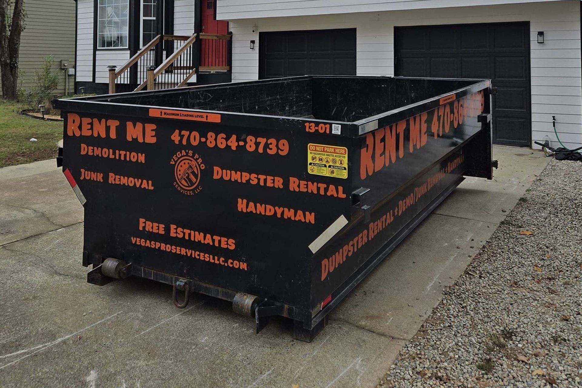 Black dumpster on a concrete driveway in front of a house. 