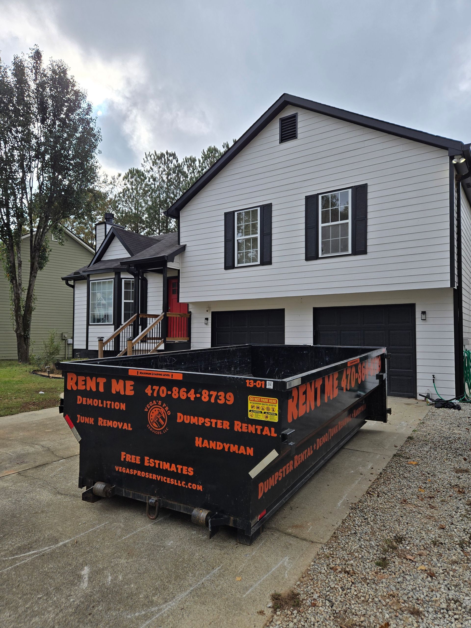 Black dumpster in front of a white two-story house with black trim and a red front door.