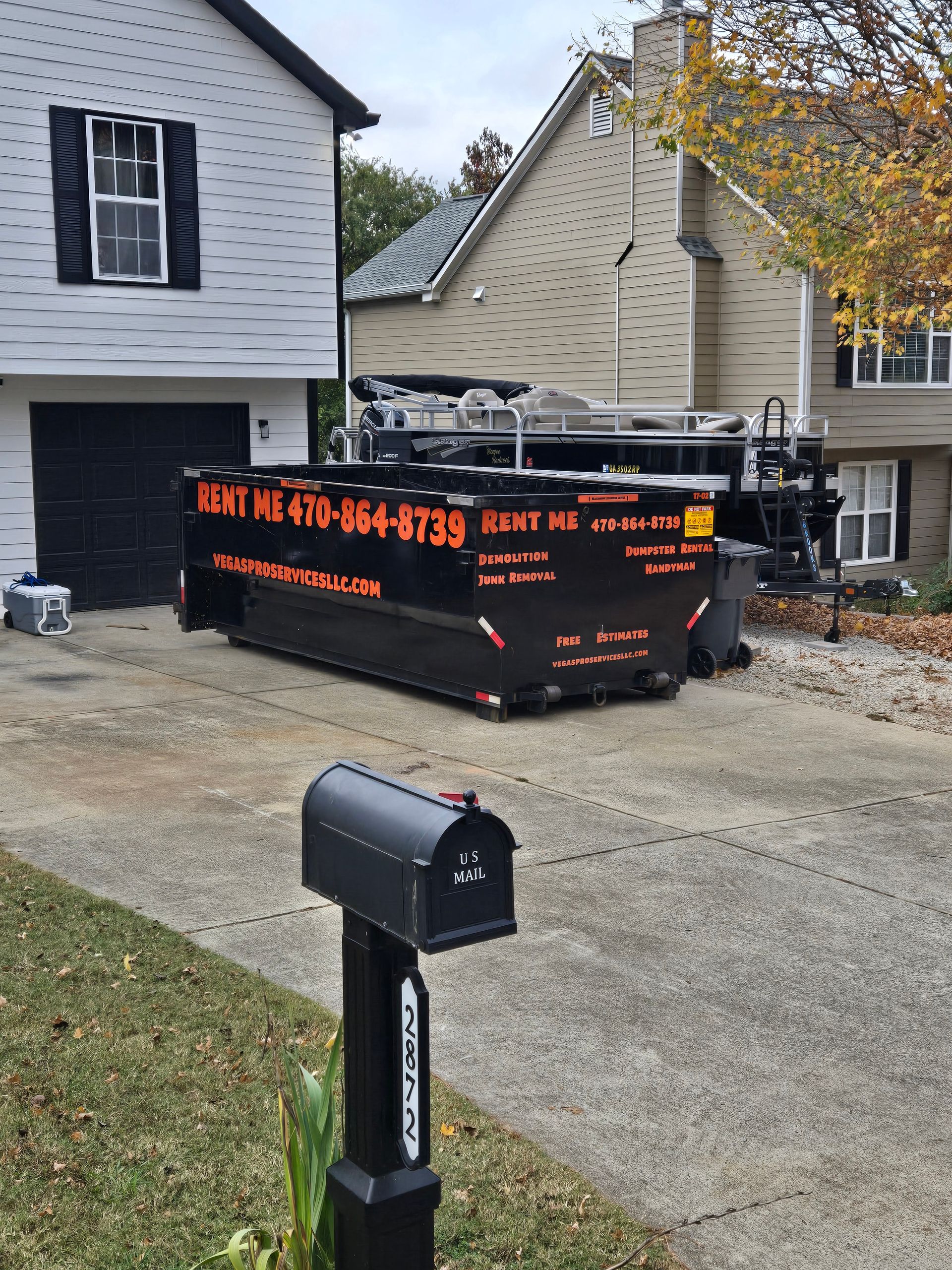 Black dumpster on a driveway in front of a house. Black mailbox in foreground.