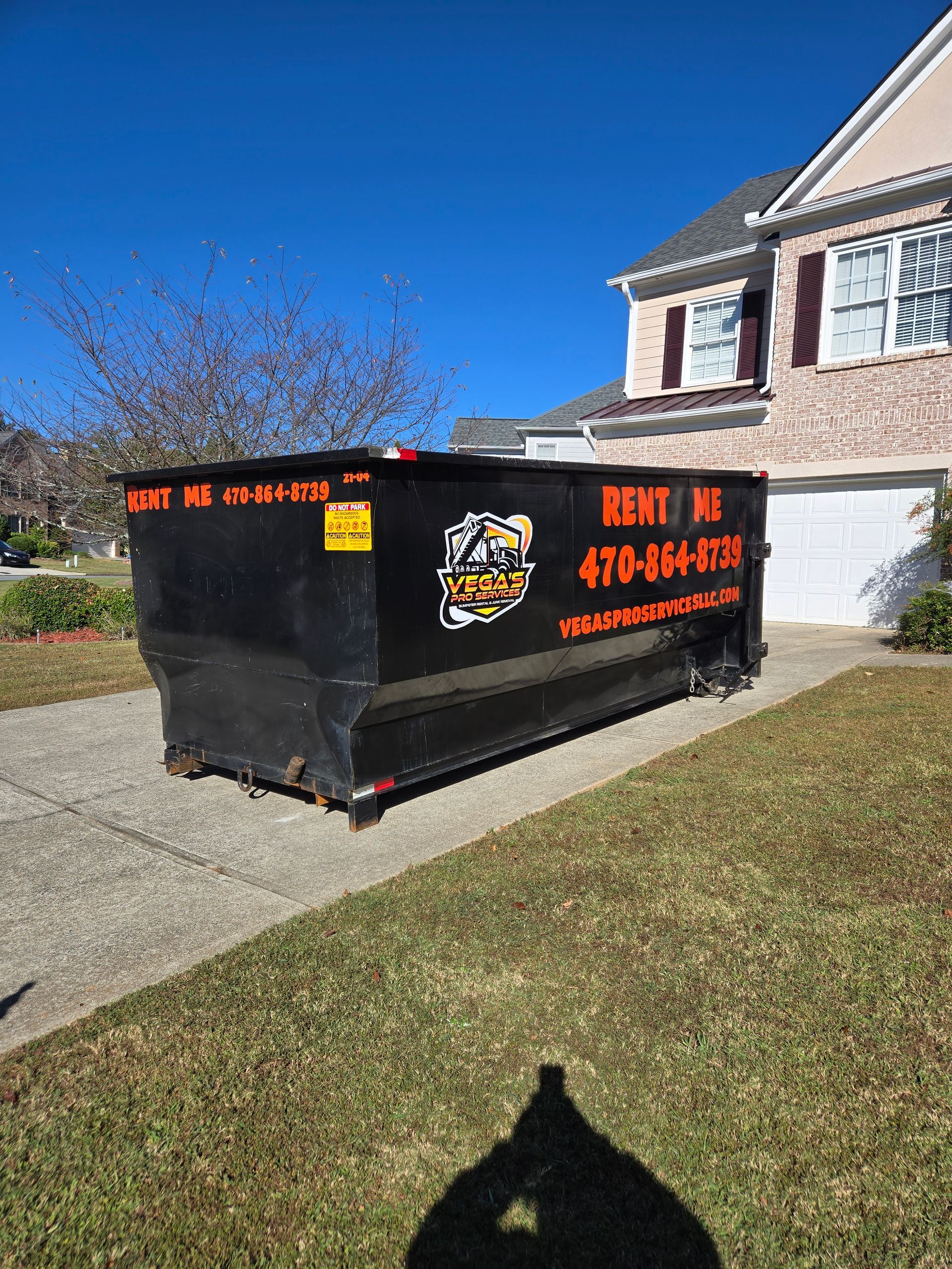Black dumpster on a driveway in front of a house, with