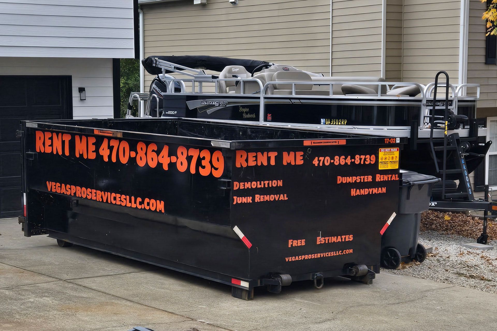 Black dumpster for rent with phone number on it. Pontoon boat in the background.