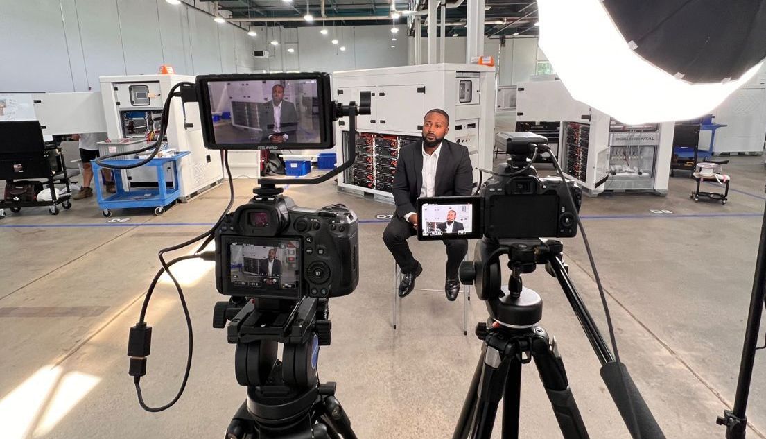 A man is sitting in front of a camera in a factory.