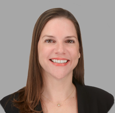 A woman wearing a black jacket and a necklace is smiling for the camera.