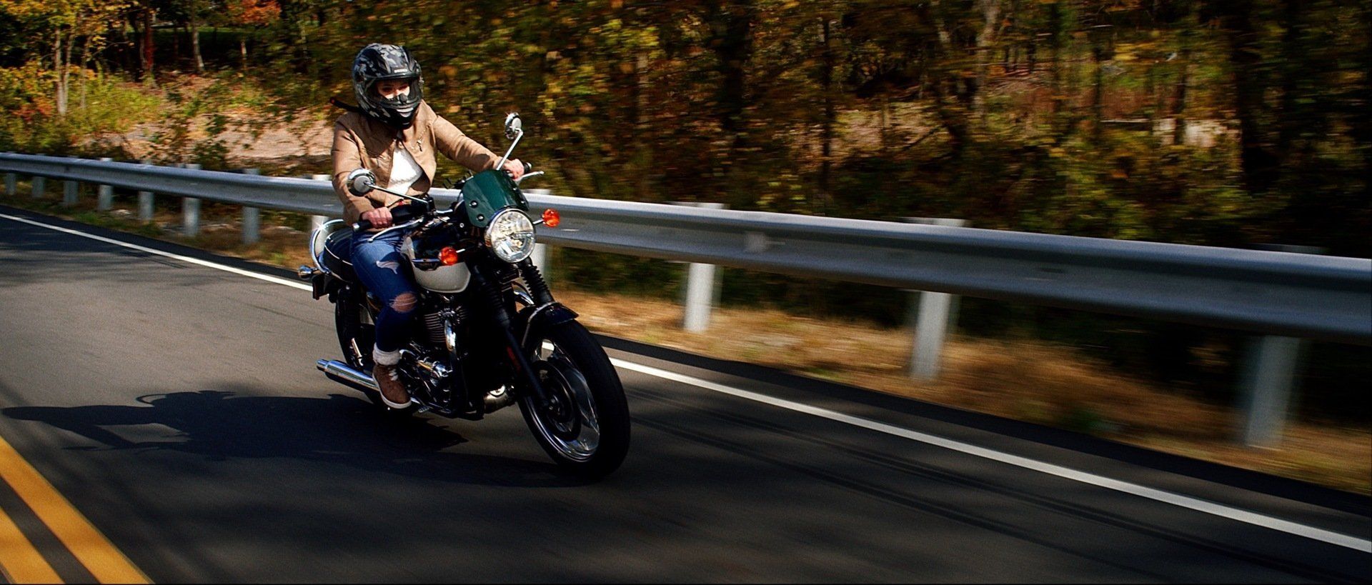 A woman is riding a motorcycle down a road.