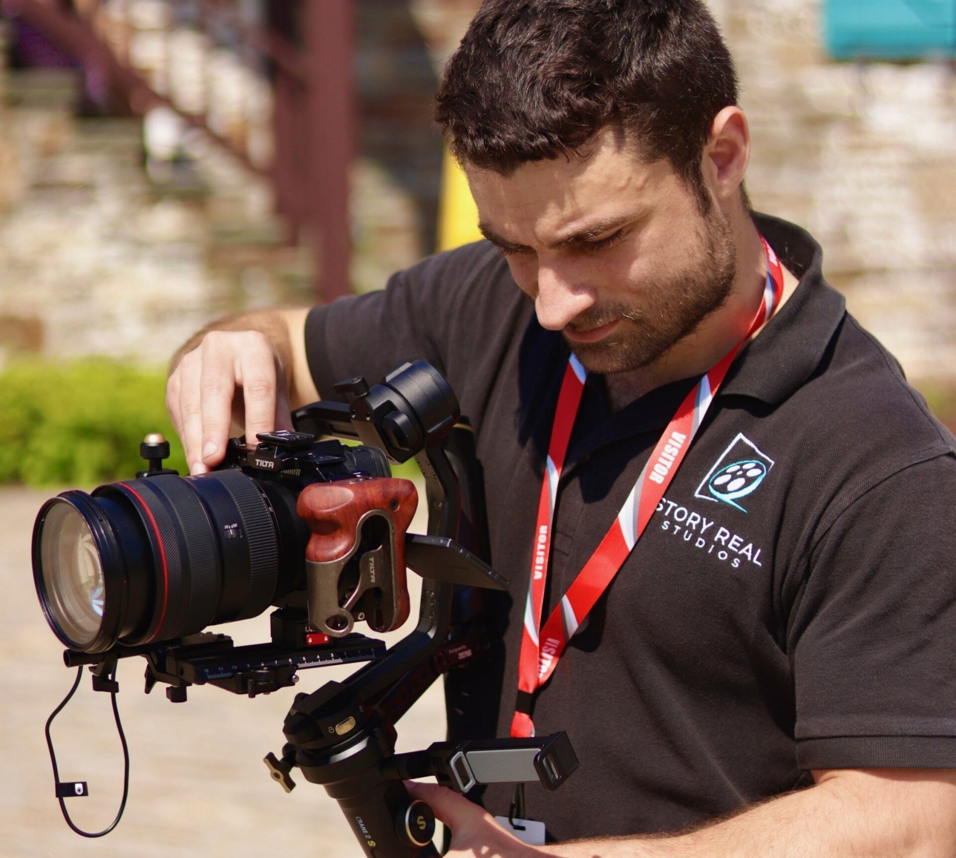A man in a story real studios shirt adjusts a camera