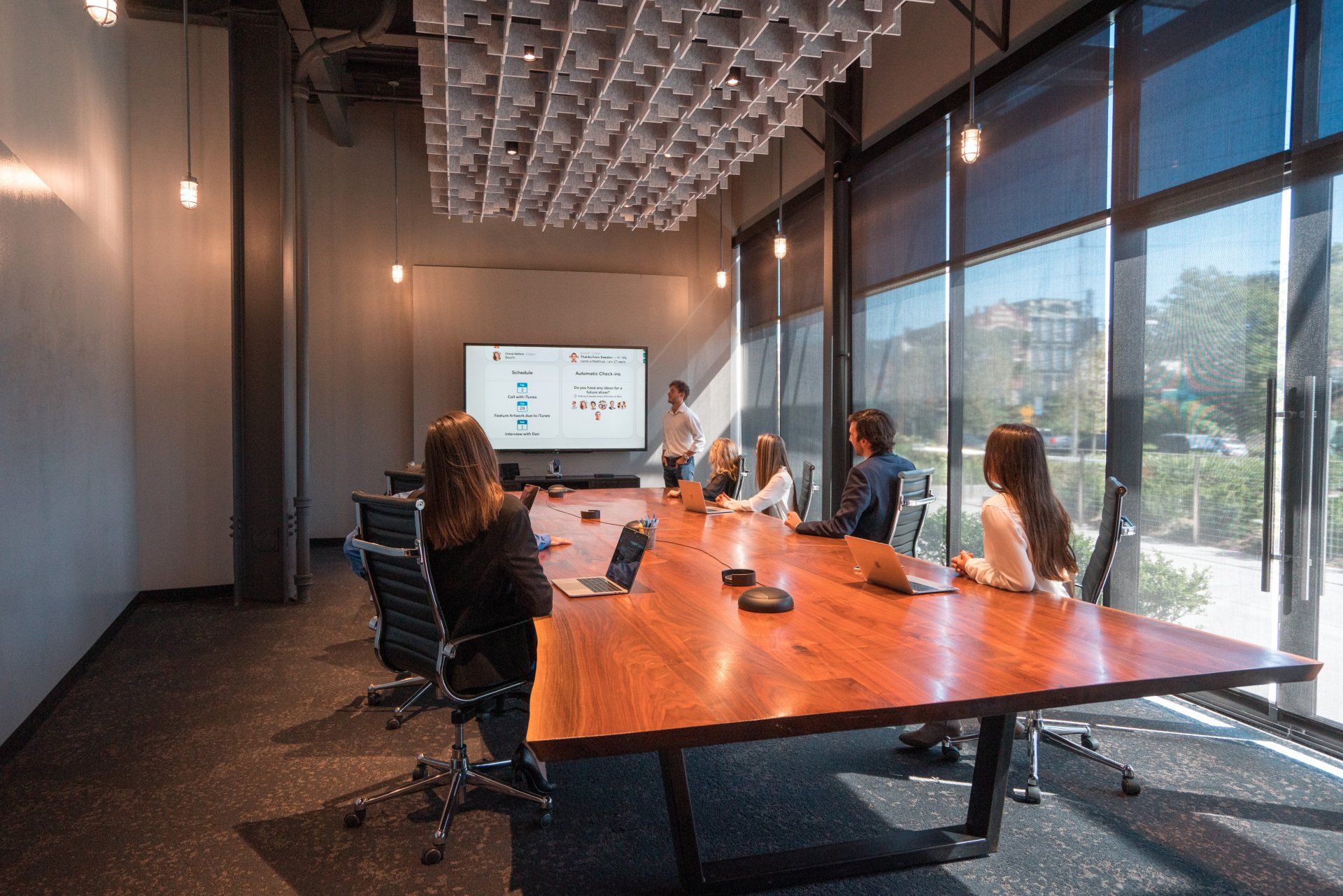 A group of people are sitting around a long wooden table in a conference room.