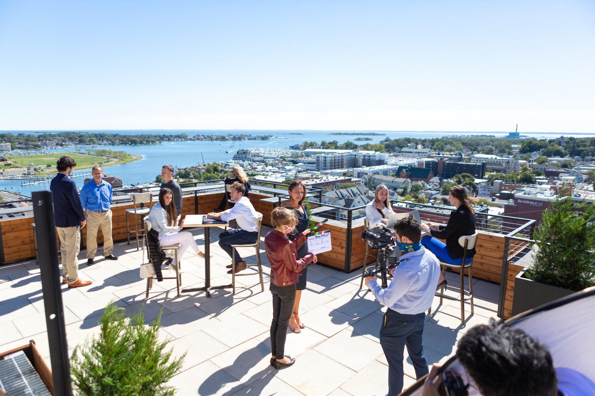 A group of people are sitting at tables on a rooftop overlooking a city.