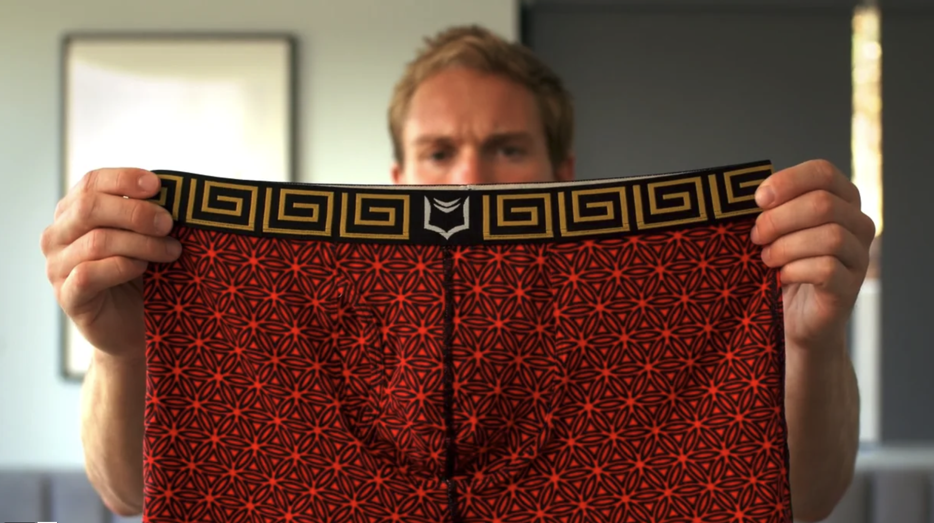 A man is holding a pair of red boxer shorts in his hands.