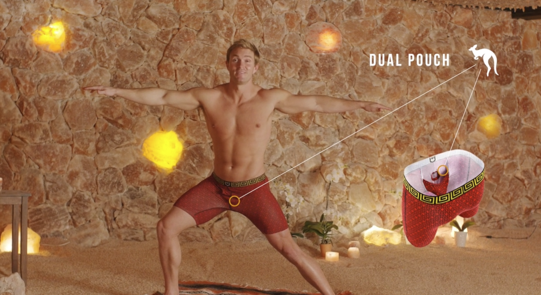 A shirtless man is doing yoga in front of a stone wall.