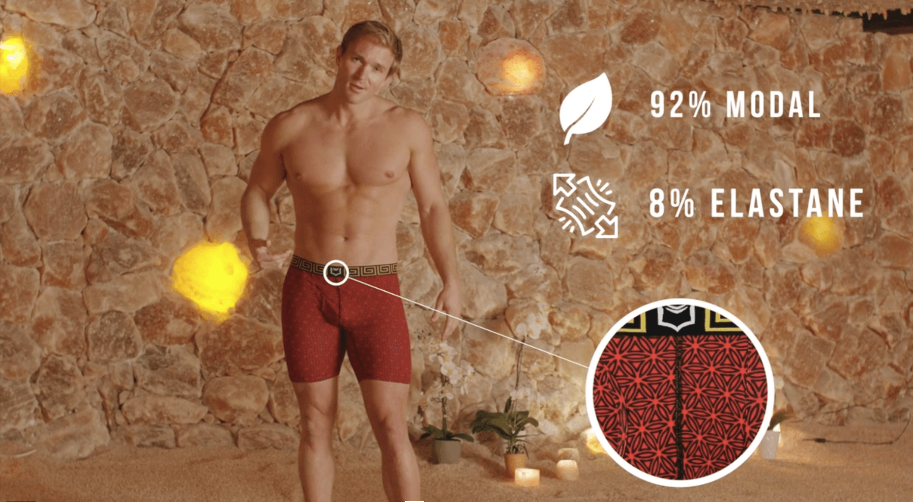 A shirtless man in red underwear is standing in front of a stone wall.
