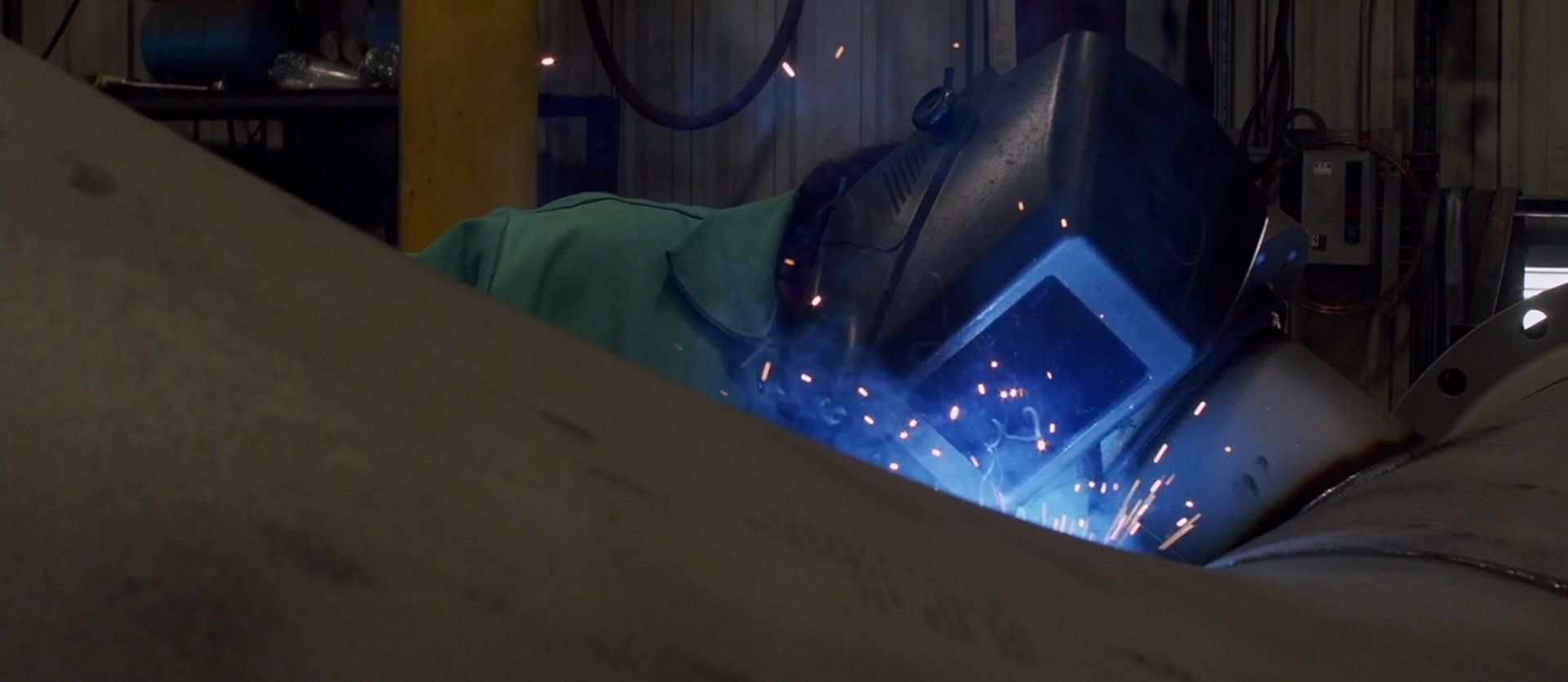 A man is welding a piece of metal in a factory.