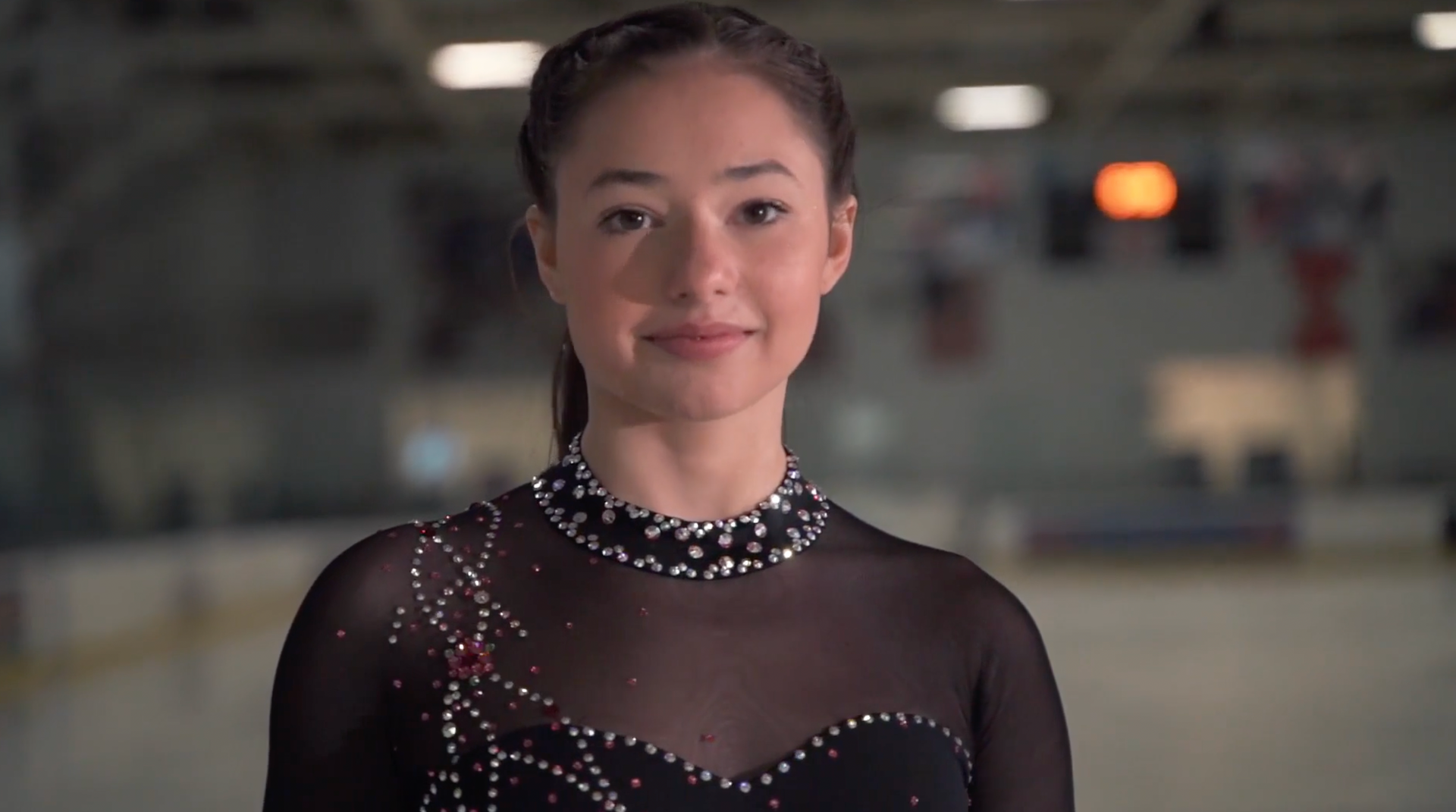 A young woman in a black dress is standing on a ice rink.